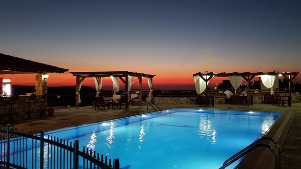 A swimming pool with a sunset view, outdoor seating, and a stone wall.