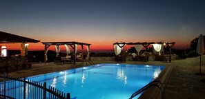 Une piscine avec vue sur le coucher de soleil, un espace extérieur aménagé et un mur en pierre.