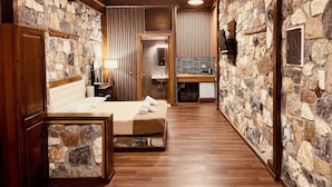 A hotel room with a stone wall, wooden floor, a bed, a nightstand, a mirror, a sink, and a small cabinet.