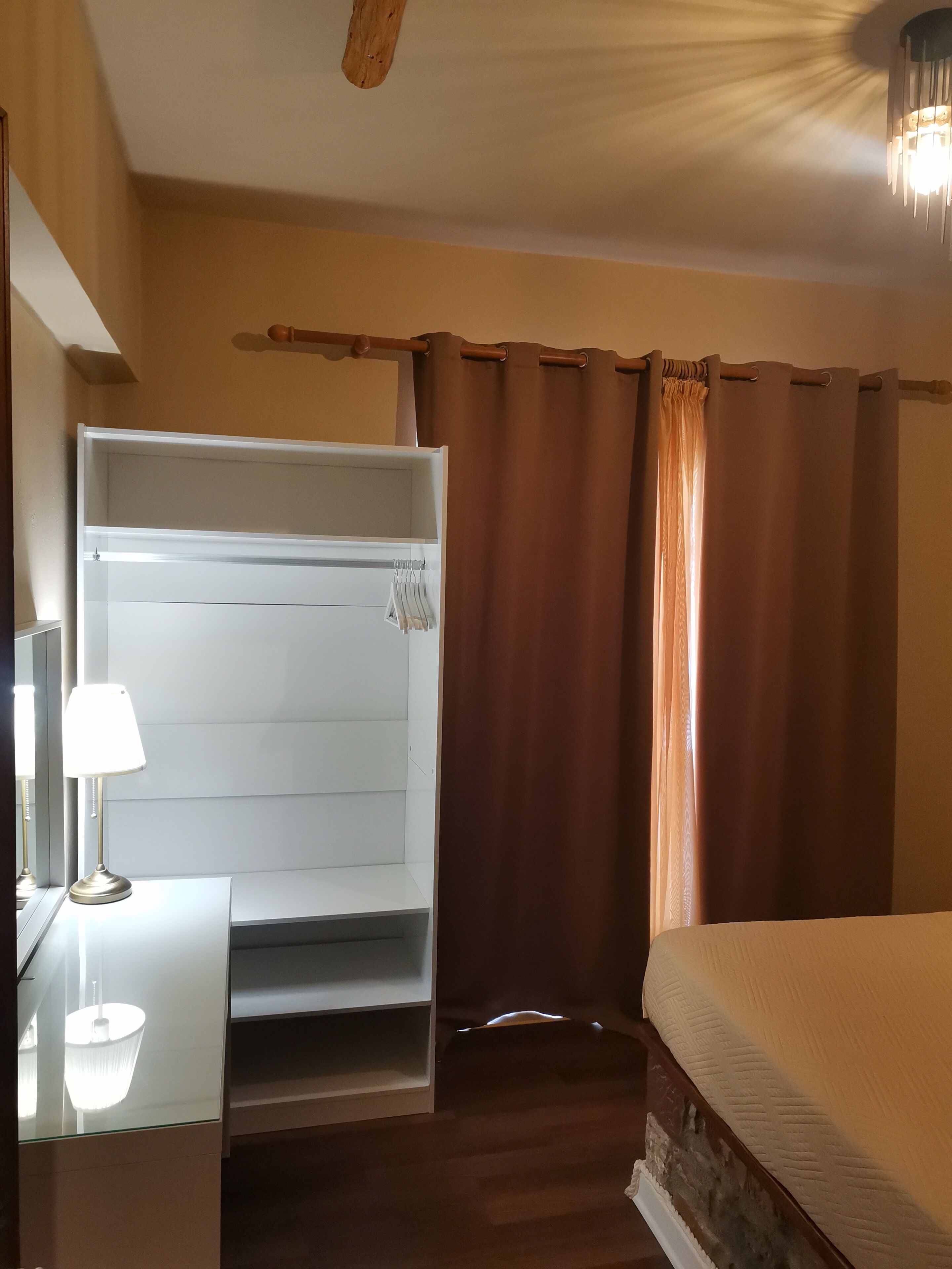Una habitación de hotel con una cama, una mesita de noche con lámpara, un armario y una cortina.