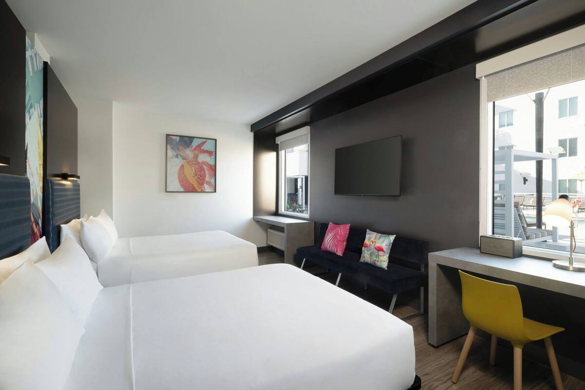 A hotel room with two beds, a desk, a chair, a TV, and a window with a city view.