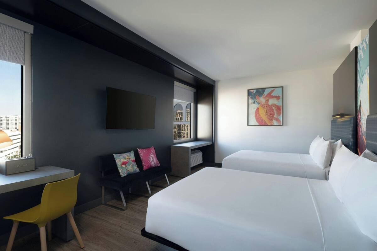 A modern hotel room with a large bed, a desk, a chair, and a TV mounted on the wall.