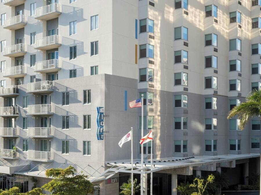 A modern hotel building with multiple floors, balconies, and a covered entrance area.