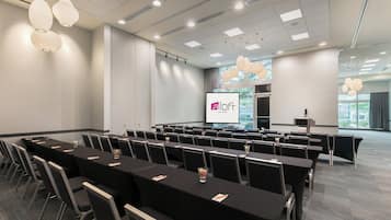 A conference room with rows of tables and chairs, a projector screen, and a presentation area.