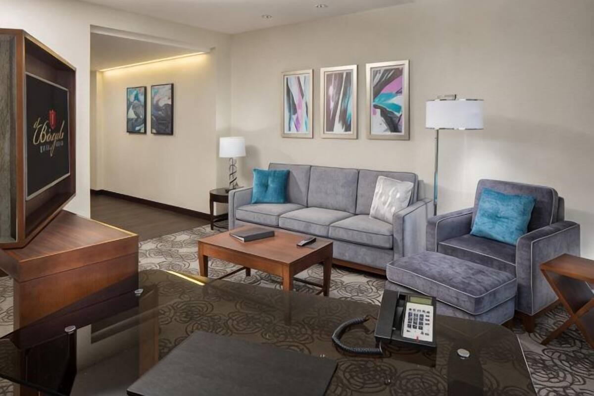 A hotel room with a sofa, armchairs, a coffee table, a TV, and a lamp.
