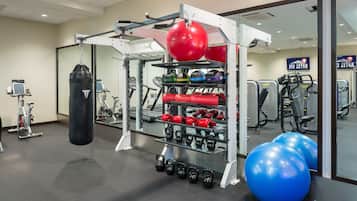 Uma academia com equipamentos de ginástica, incluindo um saco de pancada, kettlebells e bolas de exercício.