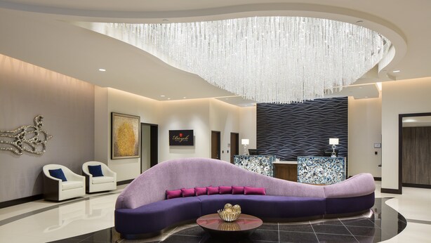 Un moderno hall de entrada con un sofá morado curvo, dos sillones blancos, una mesa de centro redonda y un techo decorativo.