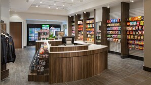 Una tienda moderna con un mostrador de recepción de madera, una variedad de aperitivos en estantes y una sección refrigerada al fondo.
