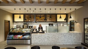 Una cafetería moderna con mostrador de mármol, lámparas colgantes negras y un refrigerador expositor.