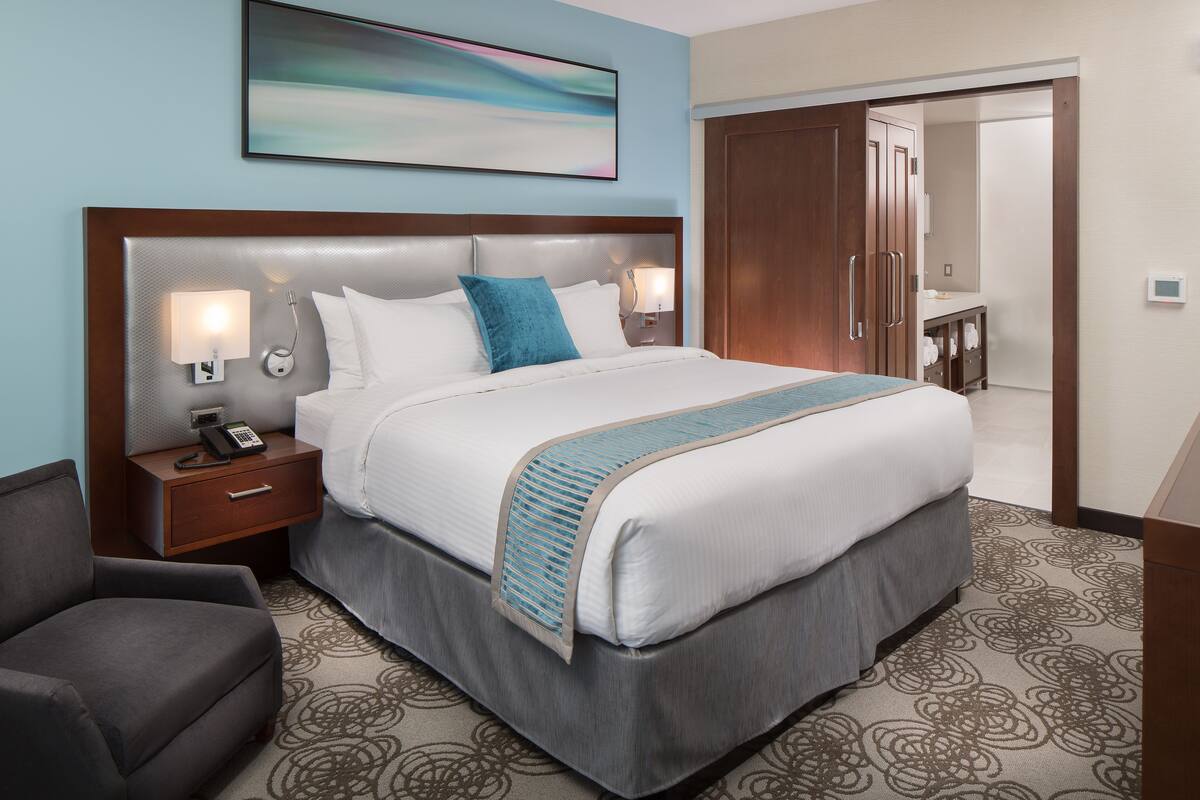A hotel room with a large bed, a nightstand with a phone, a desk, and a chair.