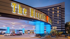 Hotel Bicycle, con fachada moderna, señalización iluminada y un estacionamiento con varios autos.