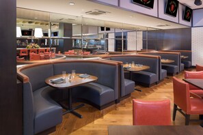 A modern restaurant with curved booths and tables, a brick wall, and a kitchen area visible through glass partitions. - Parkwest Bicycle Casino (Bell Gardens)