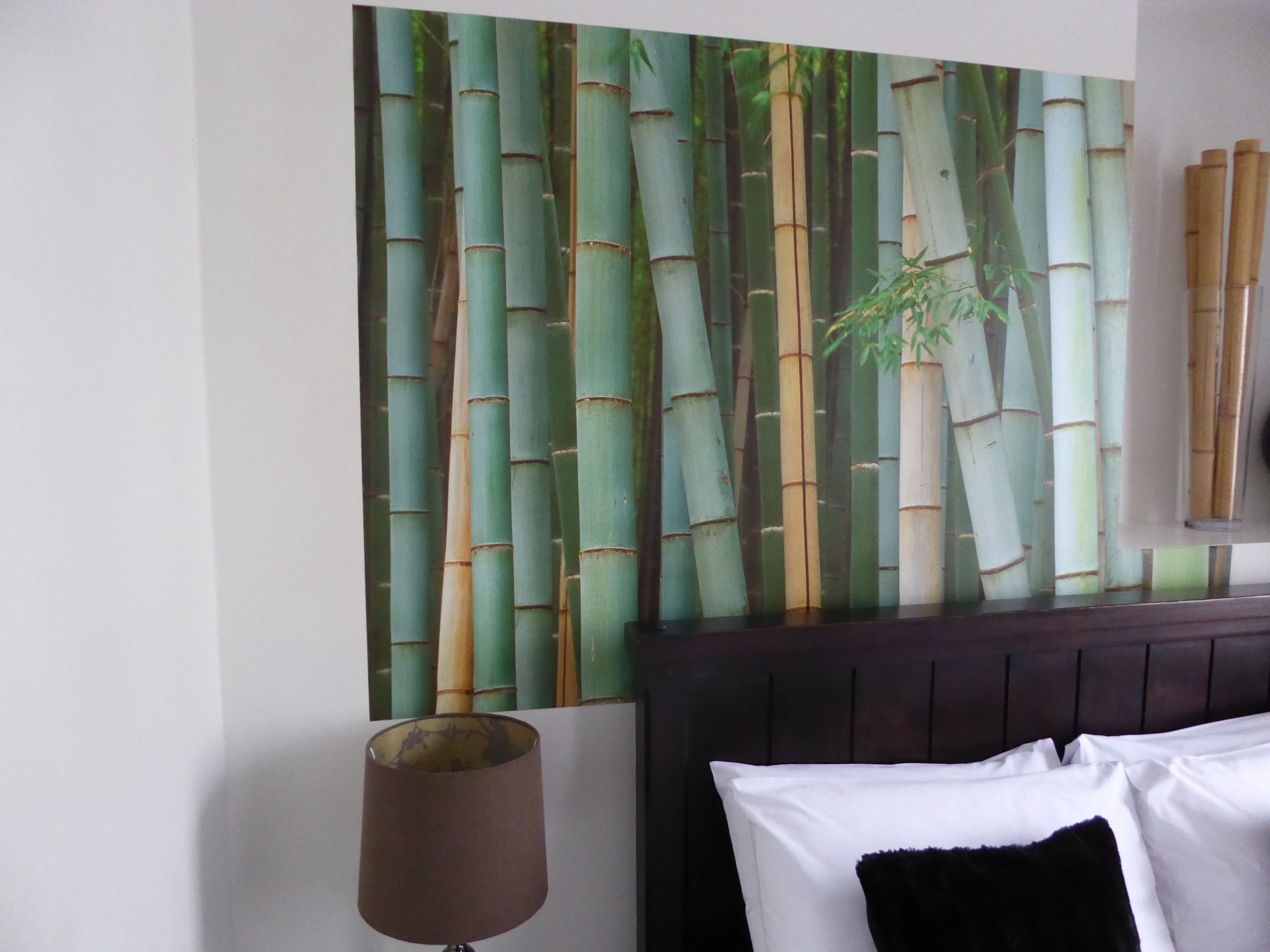 Un dormitorio con un gran mural de bambú, cabecero oscuro y una lámpara de noche.