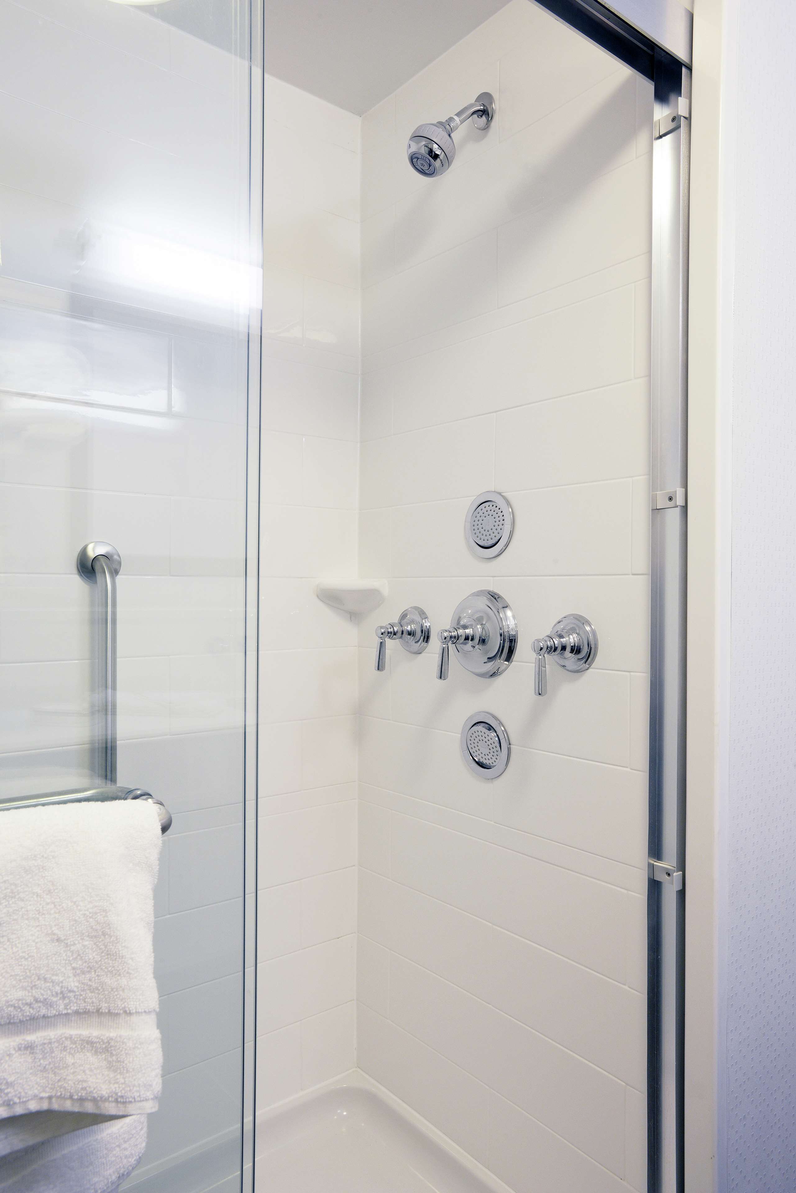 Une douche entièrementClose avec des parois en verre, un mur recouvert de carreaux blancs, une porte en verre et une serviette blanche accrochée à la porte.
