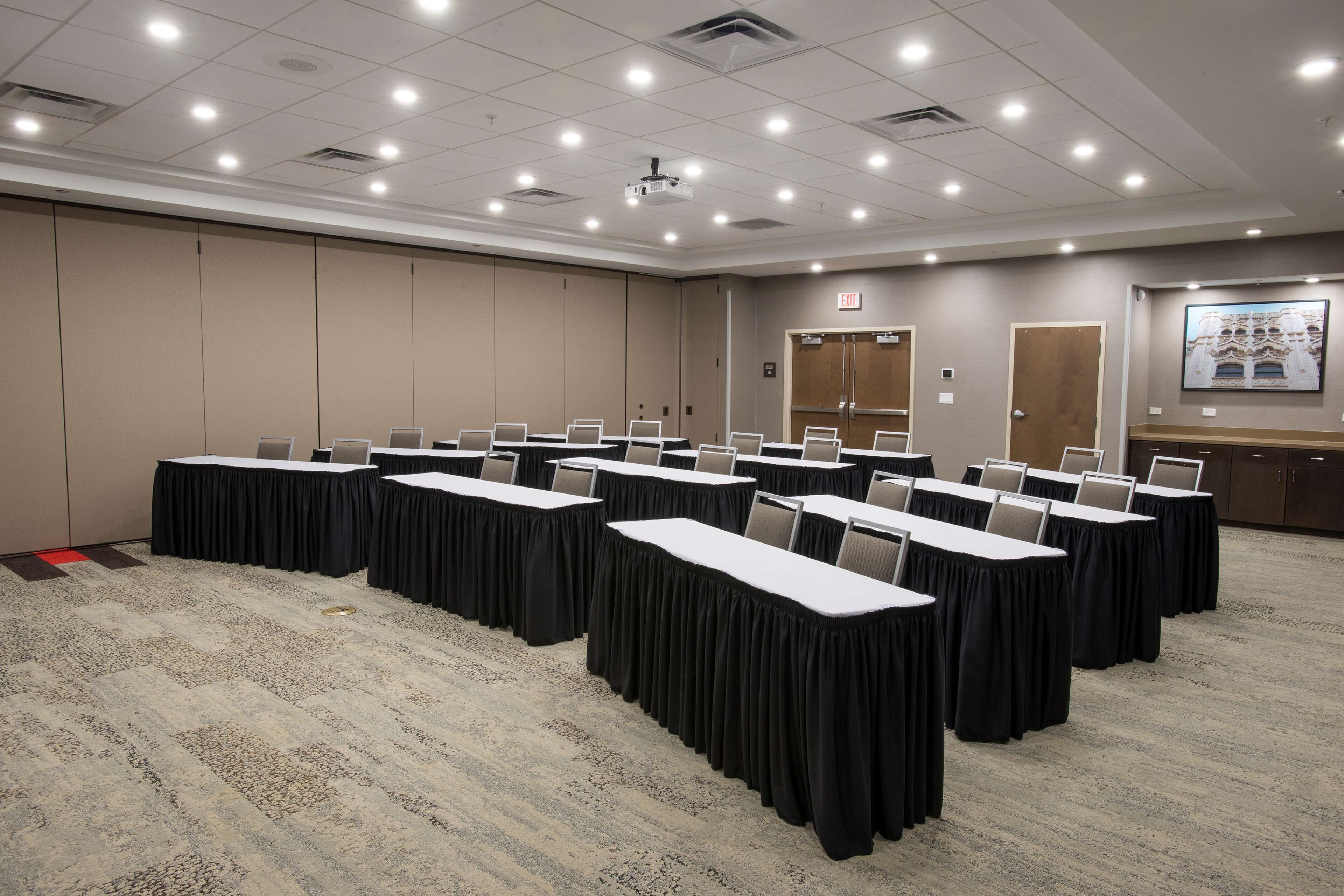 Une salle de conférence dotée de plusieurs tables, de chaises et d’un sol recouvert de moquette.