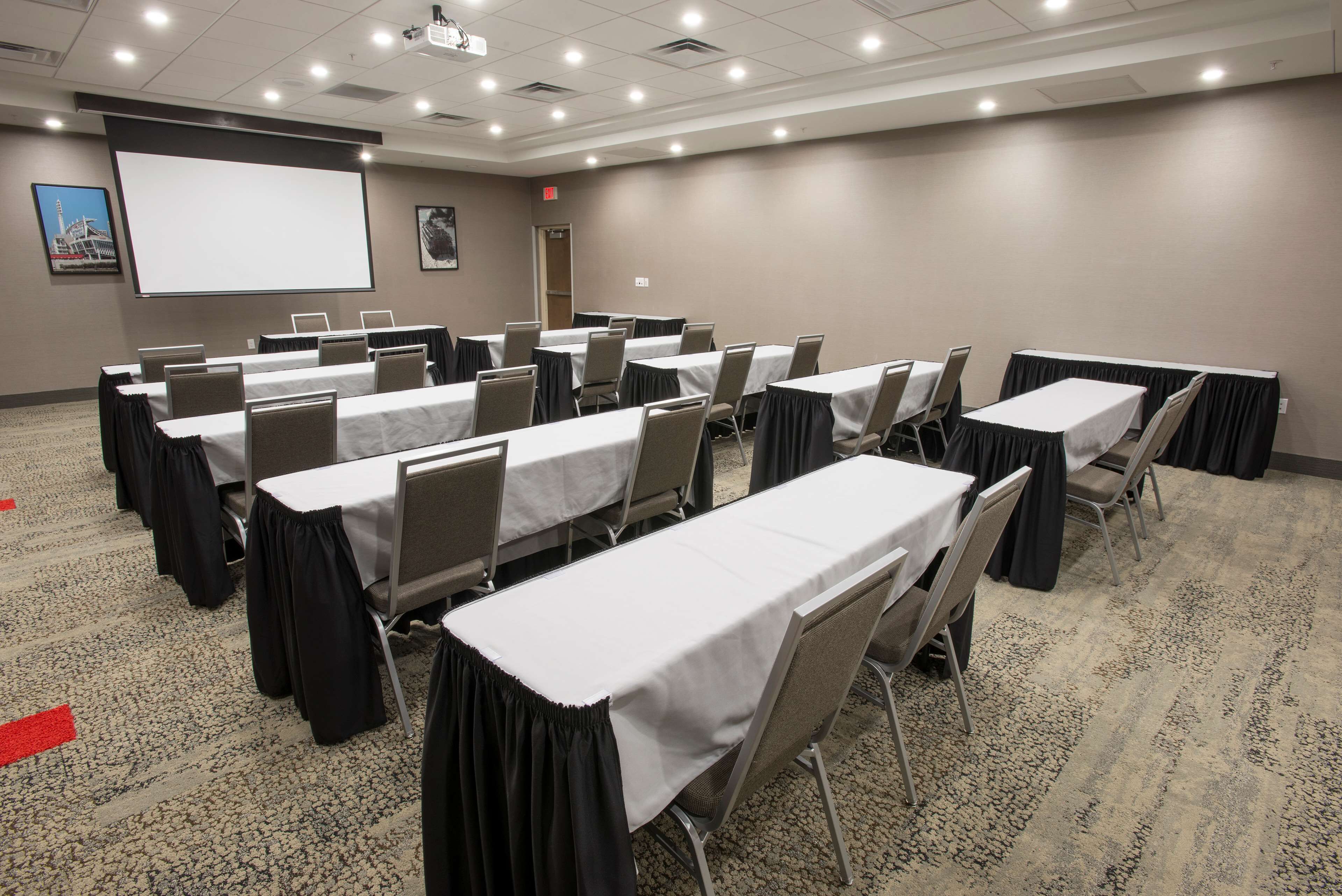 A conference room with multiple tables, chairs, a projector screen, and a carpeted floor.