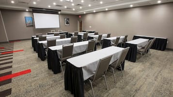 Una sala de conferencias con varias mesas y sillas, una pantalla de proyector y suelo alfombrado.