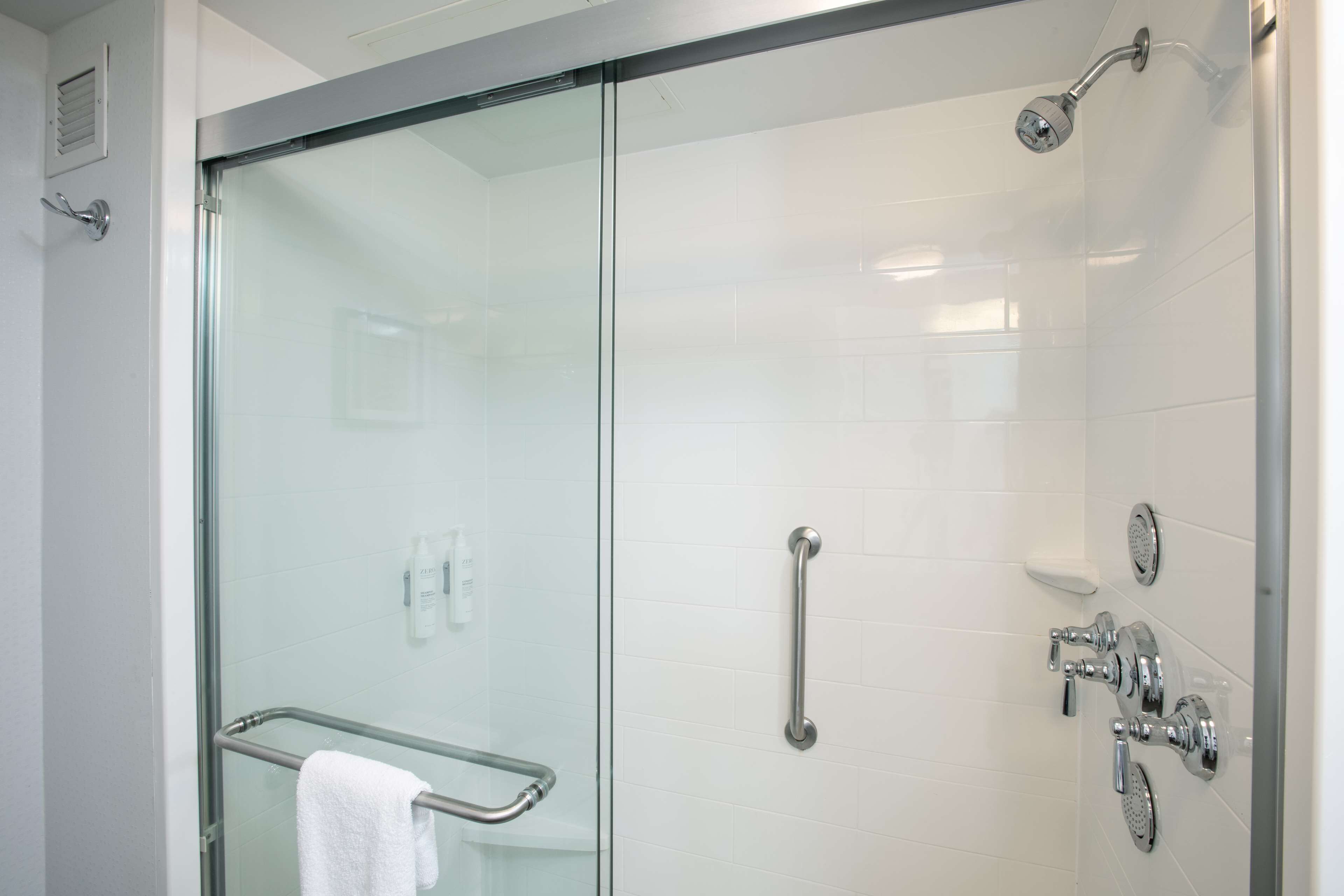 Een moderne badkamer met een douchecabine van glas, een handgreep, een handdoekhouder en een douchekop die aan de muur is bevestigd.