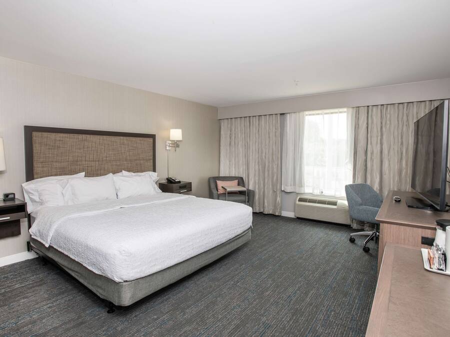 A hotel room with a large bed, a desk with a computer, a chair, a TV, and a window with curtains.