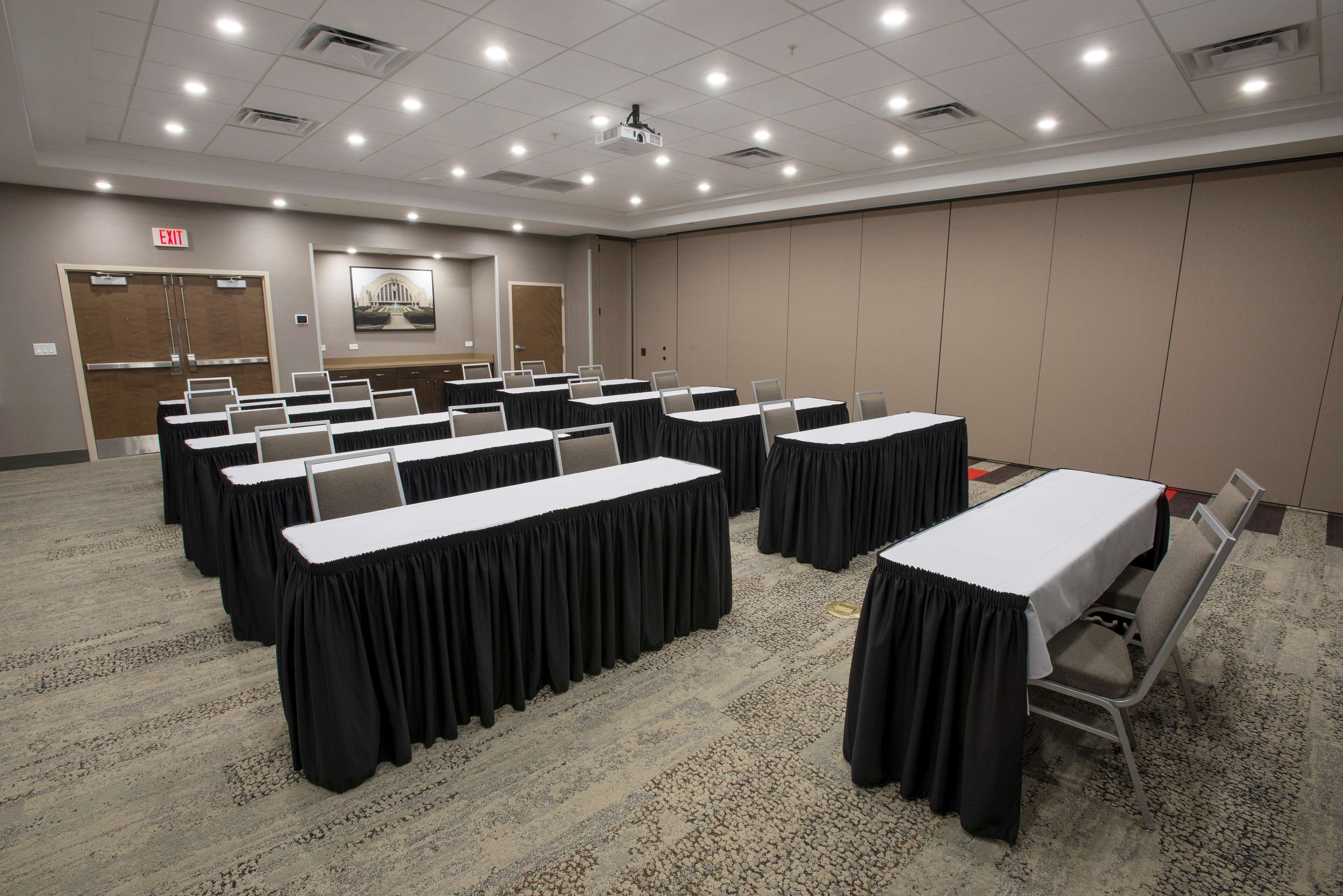 A conference room with multiple tables, chairs, and a projector screen.