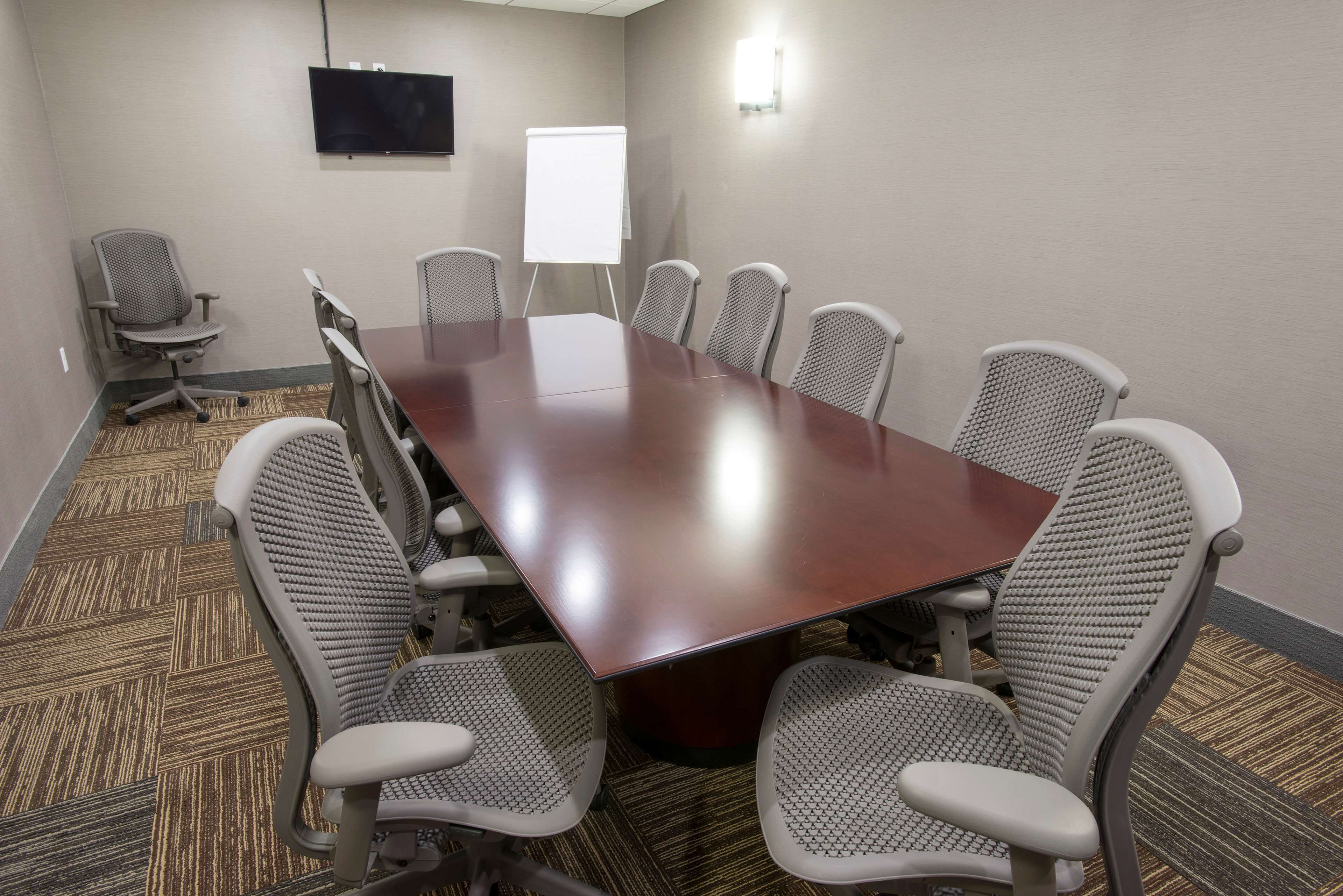 Un salón de conferencias con una gran mesa rectangular, seis sillas de oficina, una pizarra y un televisor de pantalla plana montado en la pared.