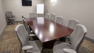 Un salón de conferencias con una gran mesa rectangular, seis sillas de oficina, una pizarra y un televisor de pantalla plana montado en la pared.