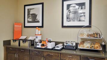 A breakfast bar with coffee machines, a coffee dispenser, and a variety of pastries.