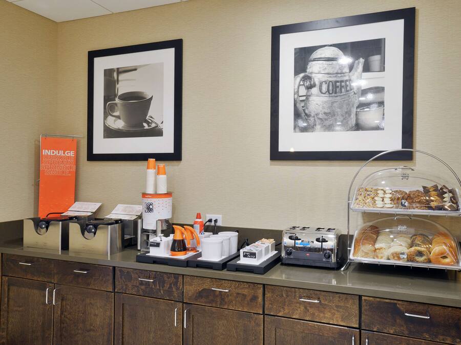 A breakfast bar with coffee machines, a coffee dispenser, and a variety of pastries.