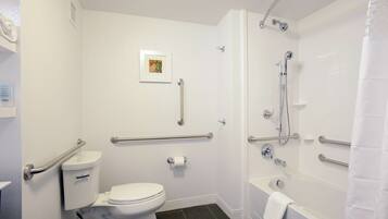 A bathroom with a toilet, a shower, and a bathtub. It includes grab bars and a picture on the wall.