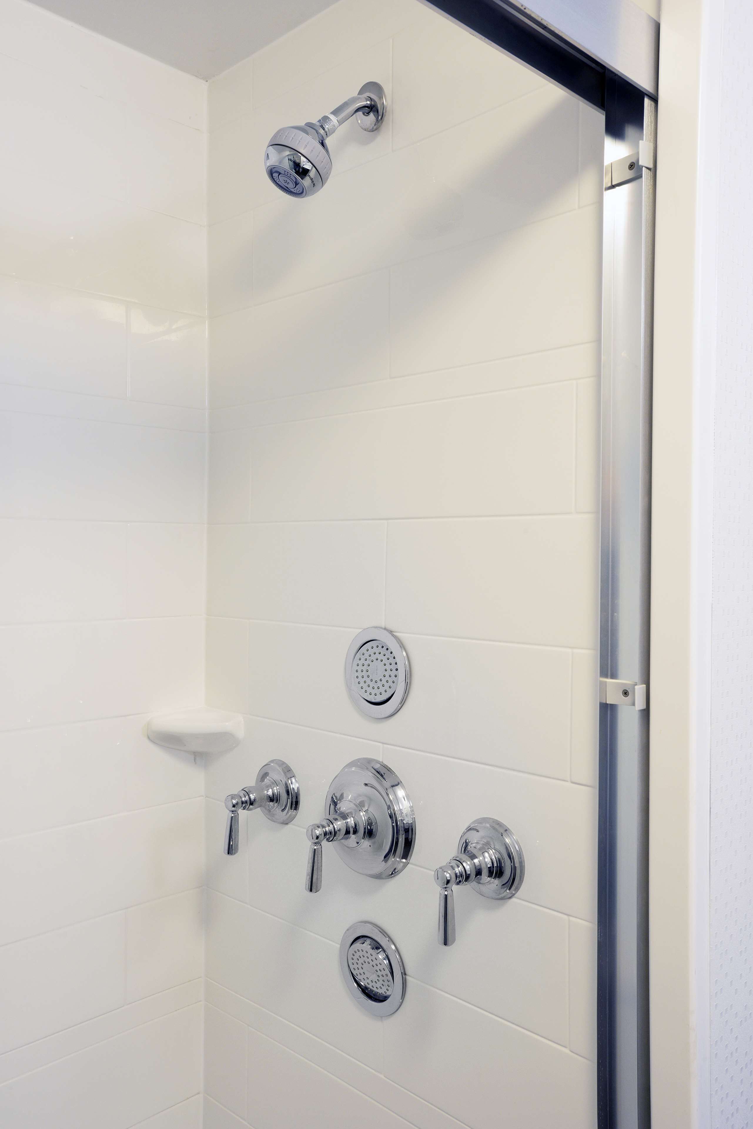 Ducha con múltiples accesorios de cromo, incluyendo un cabezal de ducha de mano y mandos instalados en la pared.