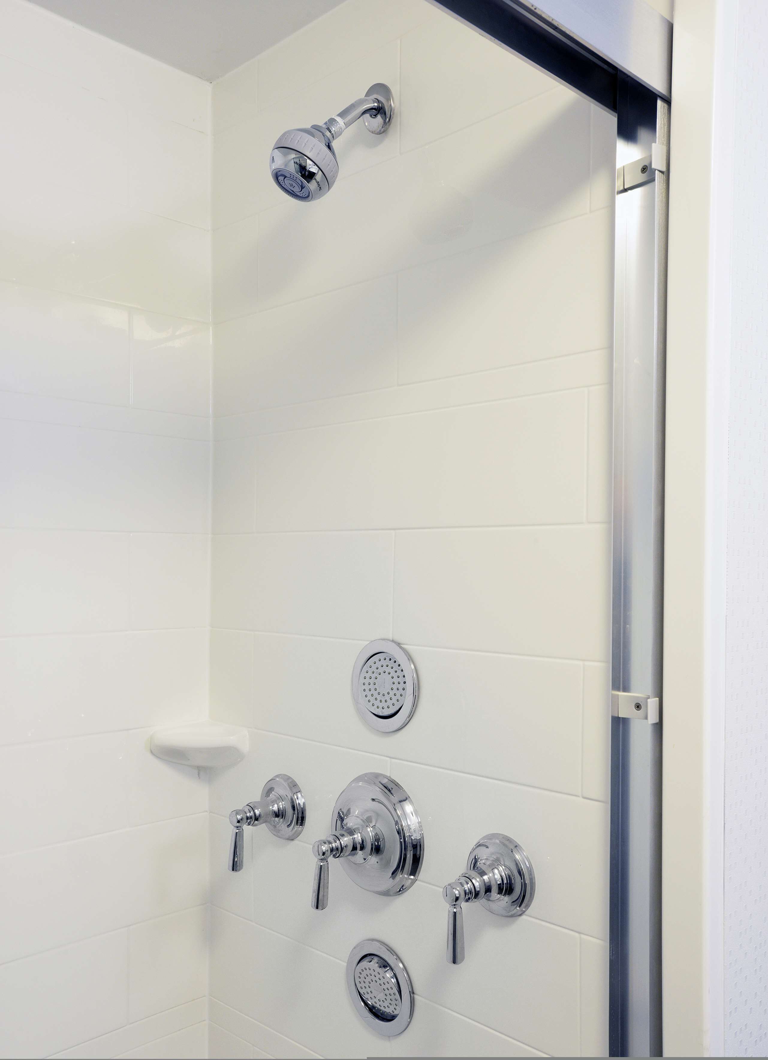 A shower with multiple chrome fixtures, including a handheld showerhead and several wall-mounted controls.