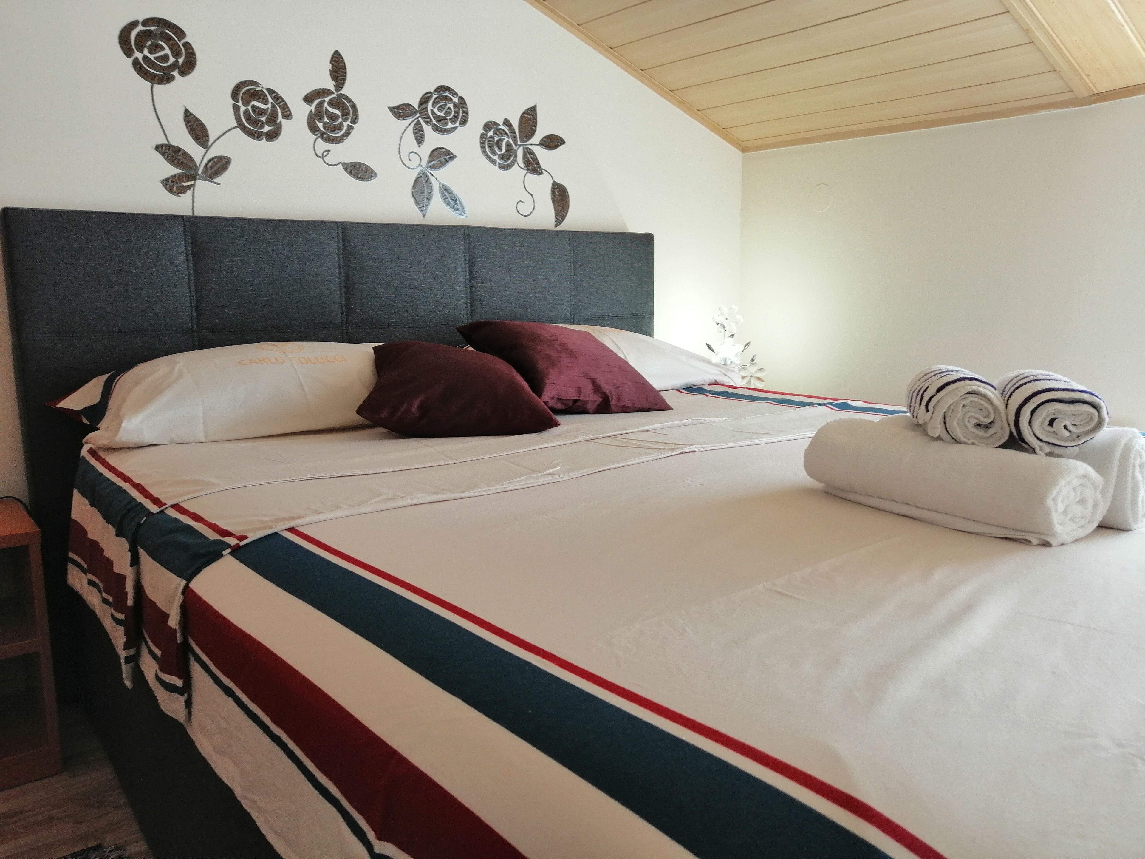 A neatly made bed with a striped bedspread, pillows, and rolled towels.