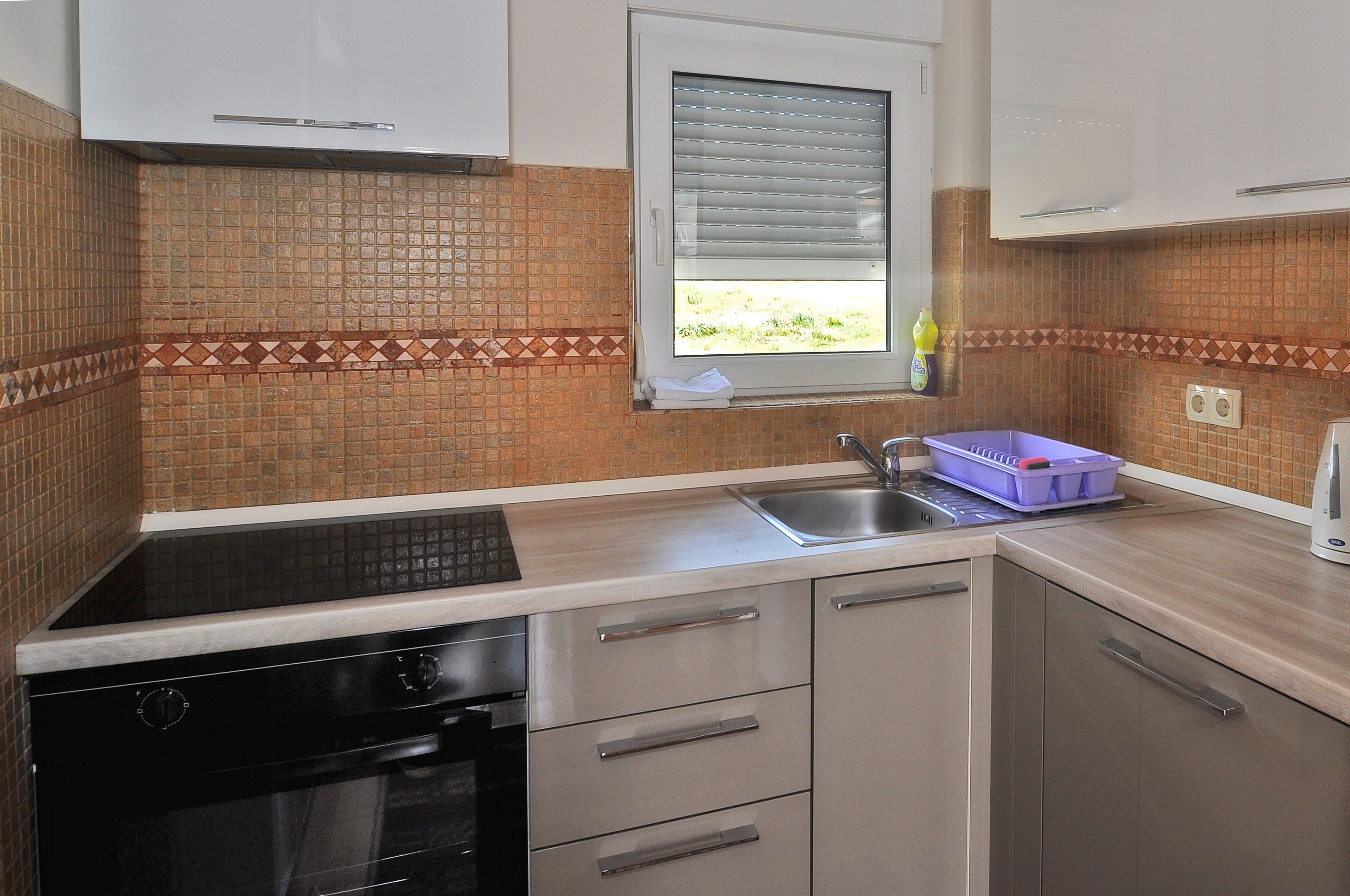 A kitchen with a black stove, a sink, and a window with blinds.