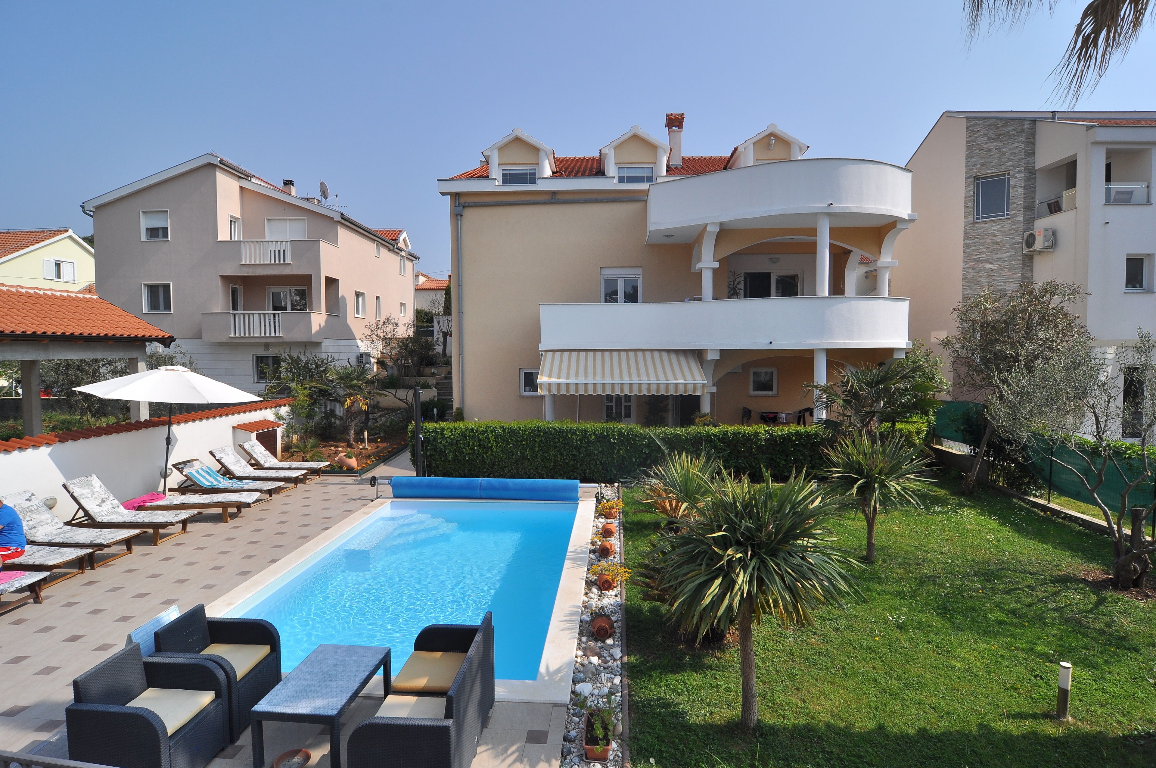 A swimming pool with lounge chairs and a small table, surrounded by greenery and adjacent buildings.