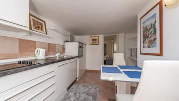 Cozinha moderna com armários brancos, bancada preta e tapete cinza. Há uma área de refeições com mesa branca e jogos americanos azuis.