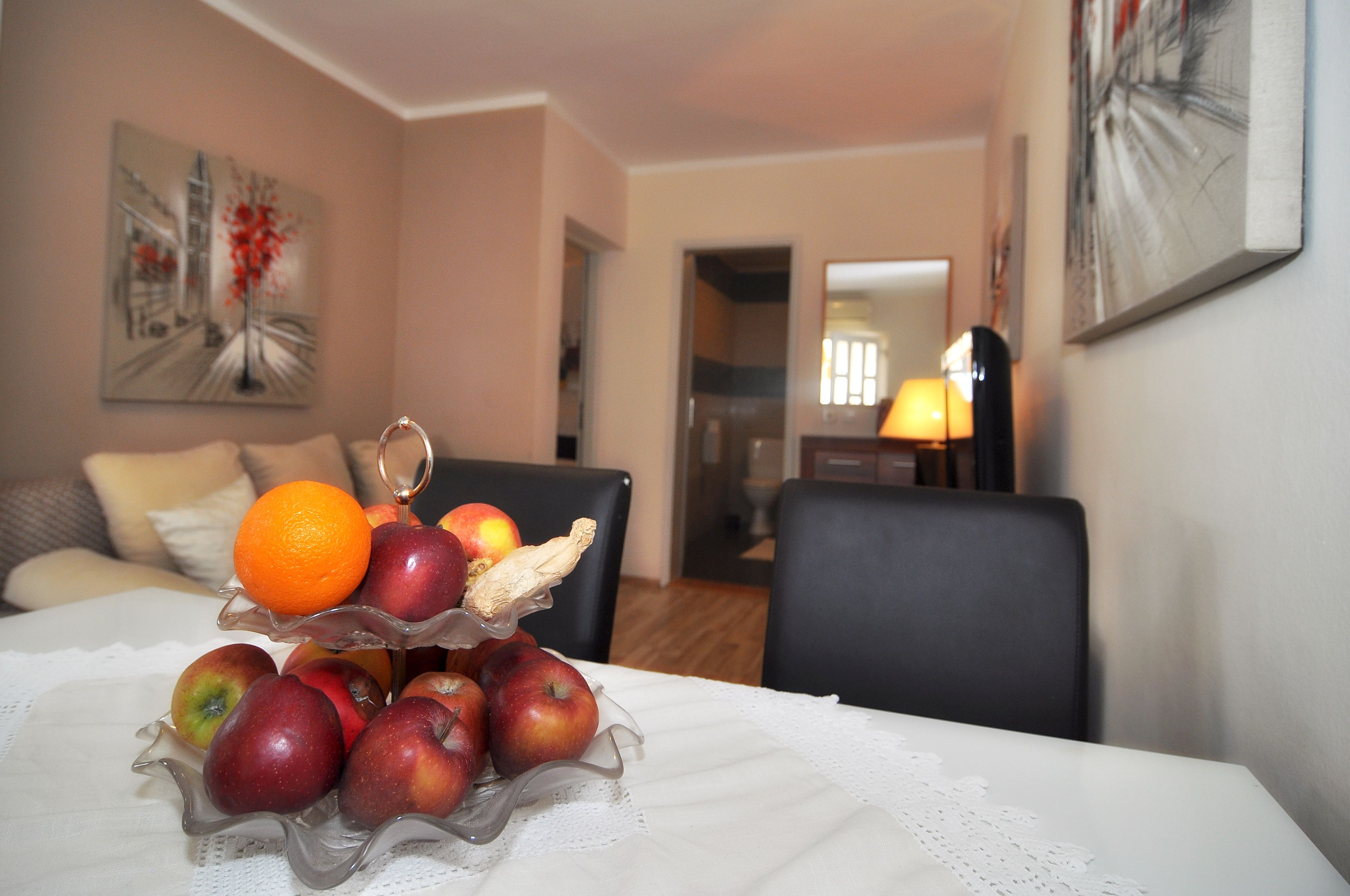 Een eettafel met een fruitmand, een bank en een lamp in een kamer met een schilderij aan de muur.