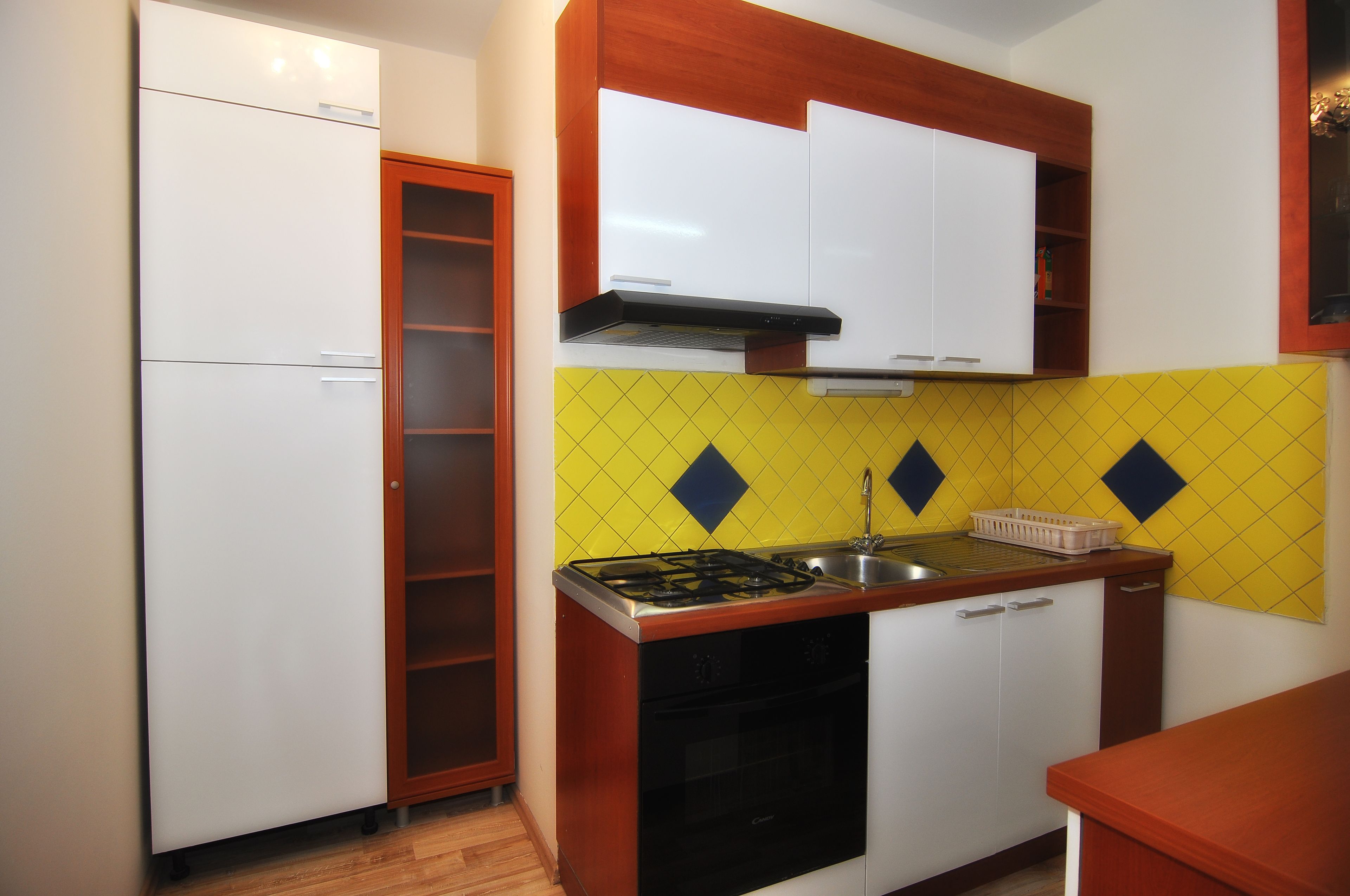 A compact kitchen with white cabinets, a yellow diamond-patterned backsplash, a gas stove, and a sink.