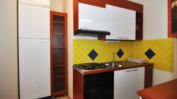 A compact kitchen with white cabinets, a yellow diamond-patterned backsplash, a gas stove, and a sink.