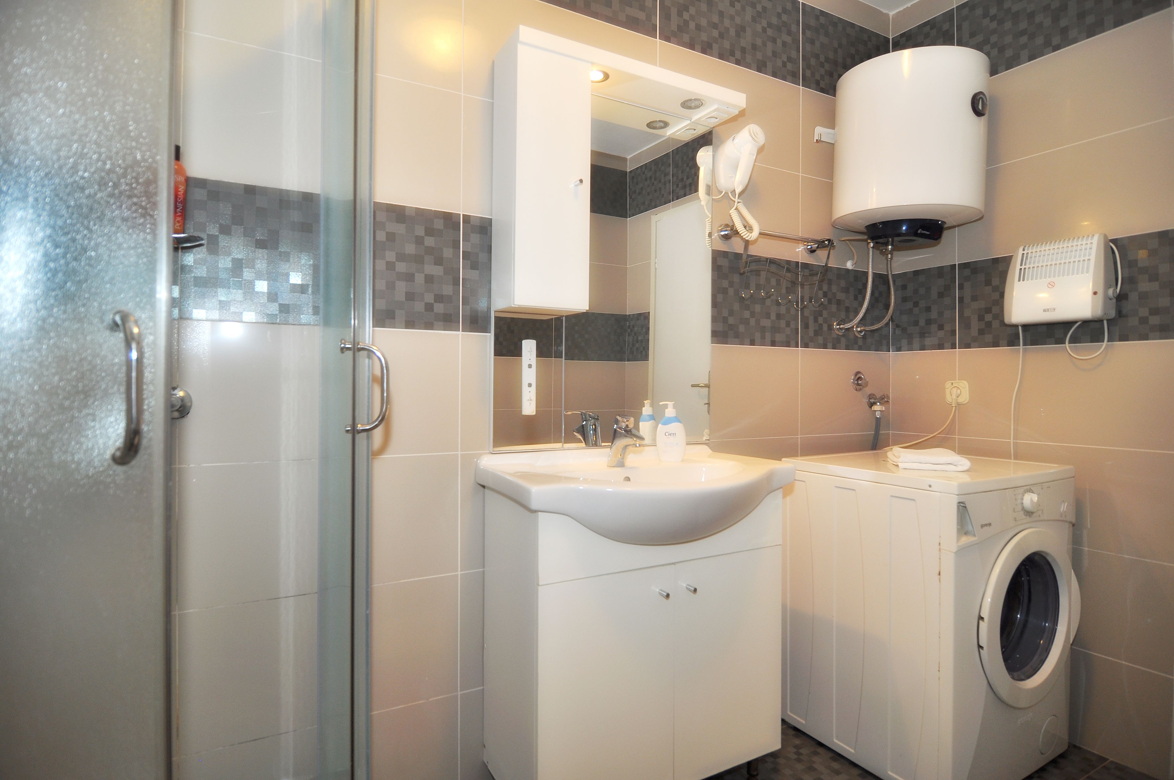A modern bathroom with a glass shower enclosure, a sink with a mirror, a built-in washing machine, and a toilet.