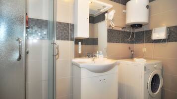 A modern bathroom with a glass shower enclosure, a sink with a mirror, a built-in washing machine, and a toilet.