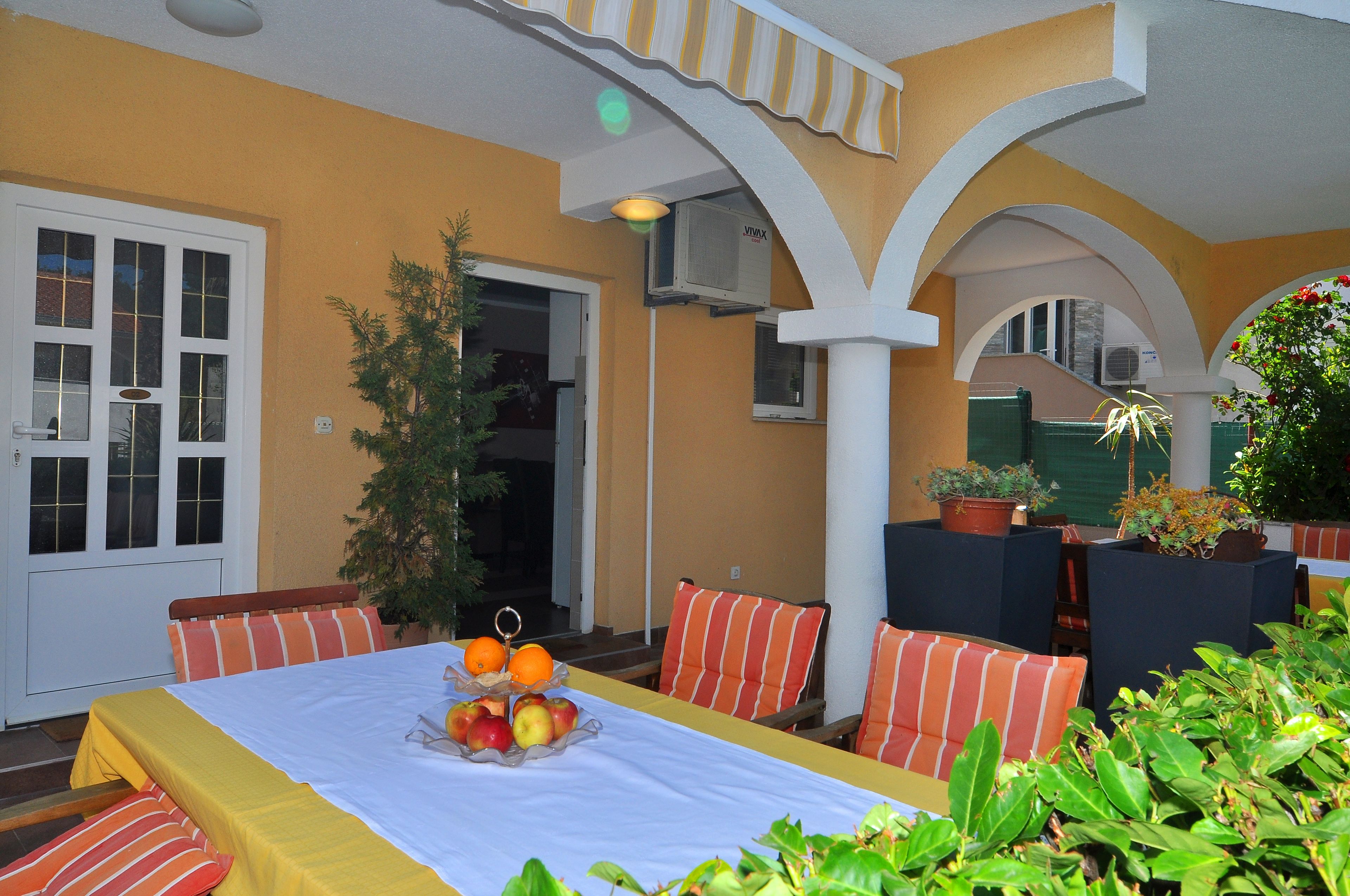 A hotel room with a bed, a dining table with fruit, striped chairs, and potted plants.