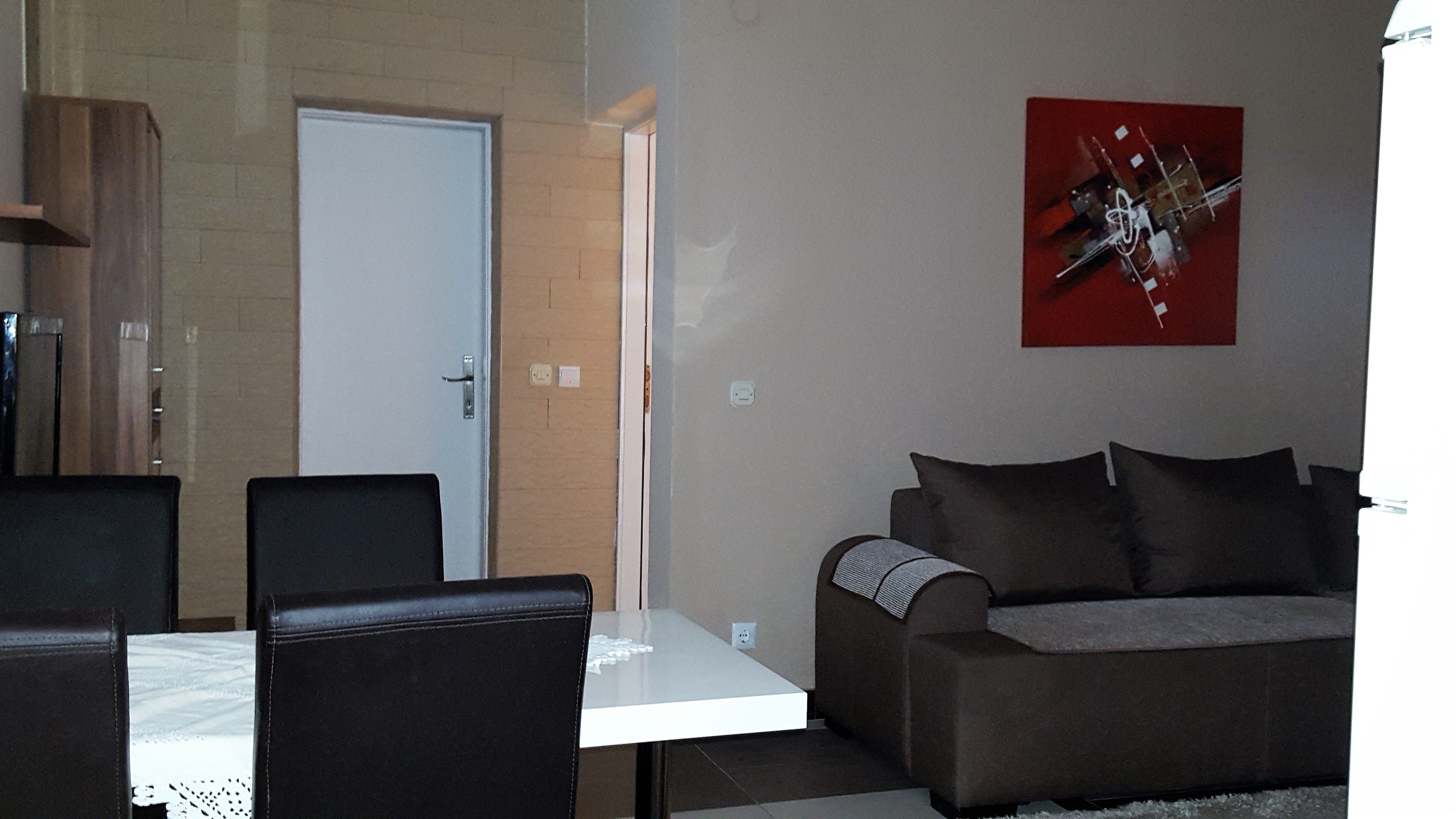 Una sala de estar con una mesa blanca, dos sillas negras, un sofá marrón y un cuadro abstracto rojo en la pared.