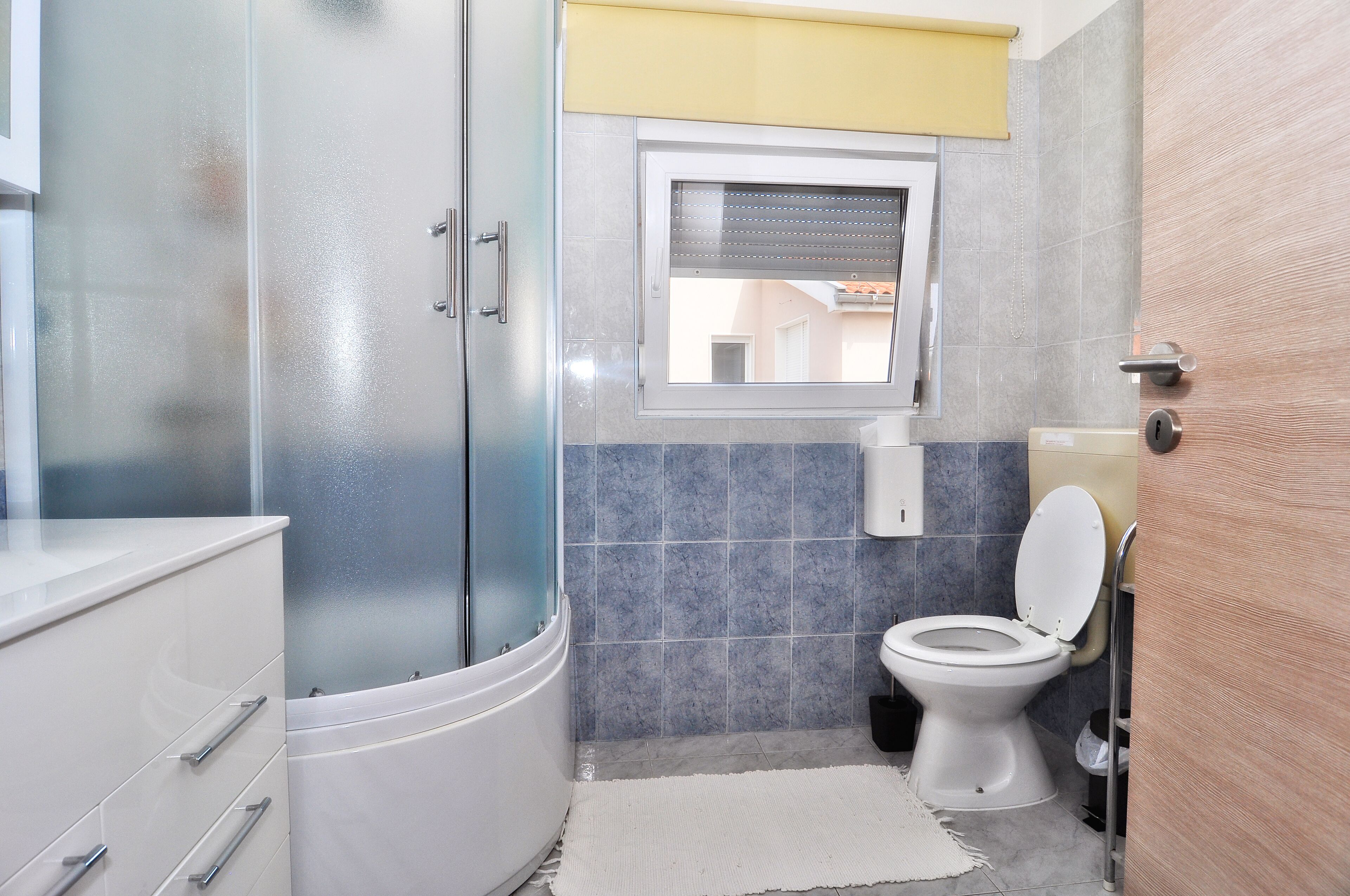 A modern bathroom with a glass shower enclosure, a toilet, and a window.