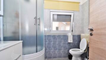 A modern bathroom with a glass shower enclosure, a toilet, and a window.