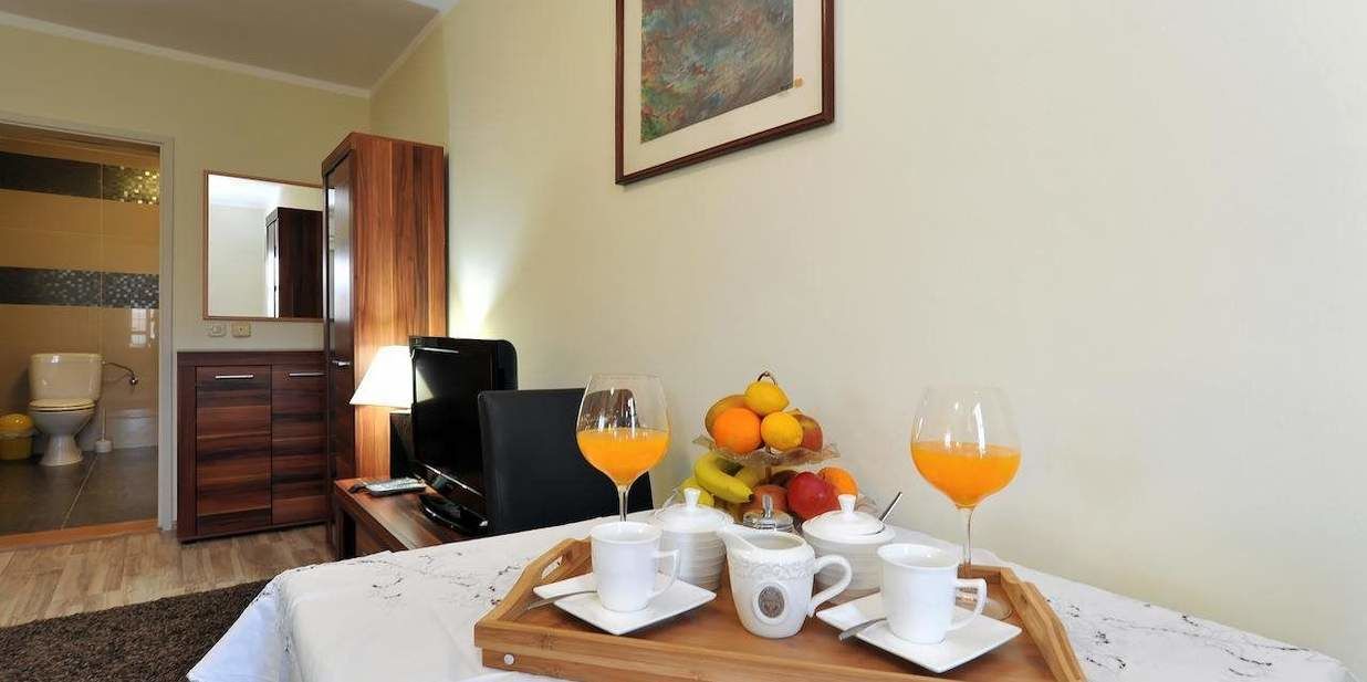 Ein Hotelzimmer mit einem Holzschrank, einem Fernseher, einem Tablett mit Frühstücksgegenständen und einer Obstschale.