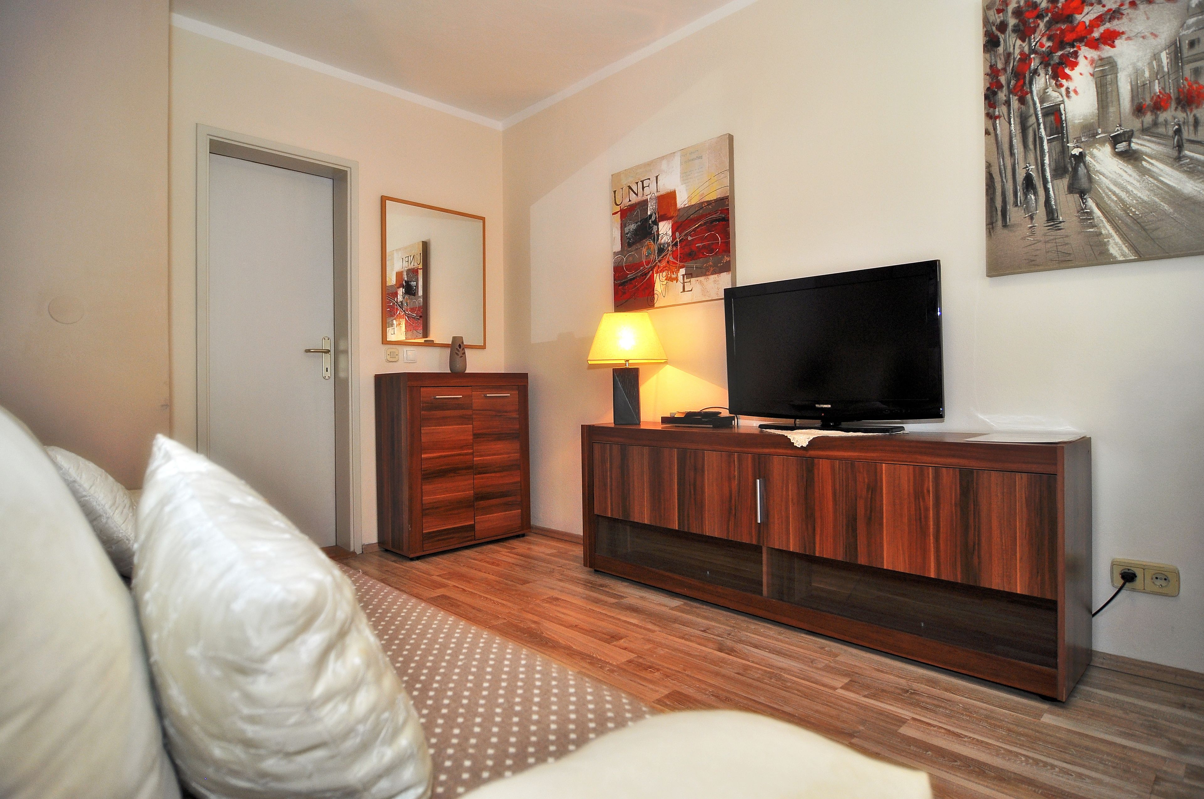 A modern living room with a wooden cabinet, a flat-screen TV, a lamp, and a painting on the wall.