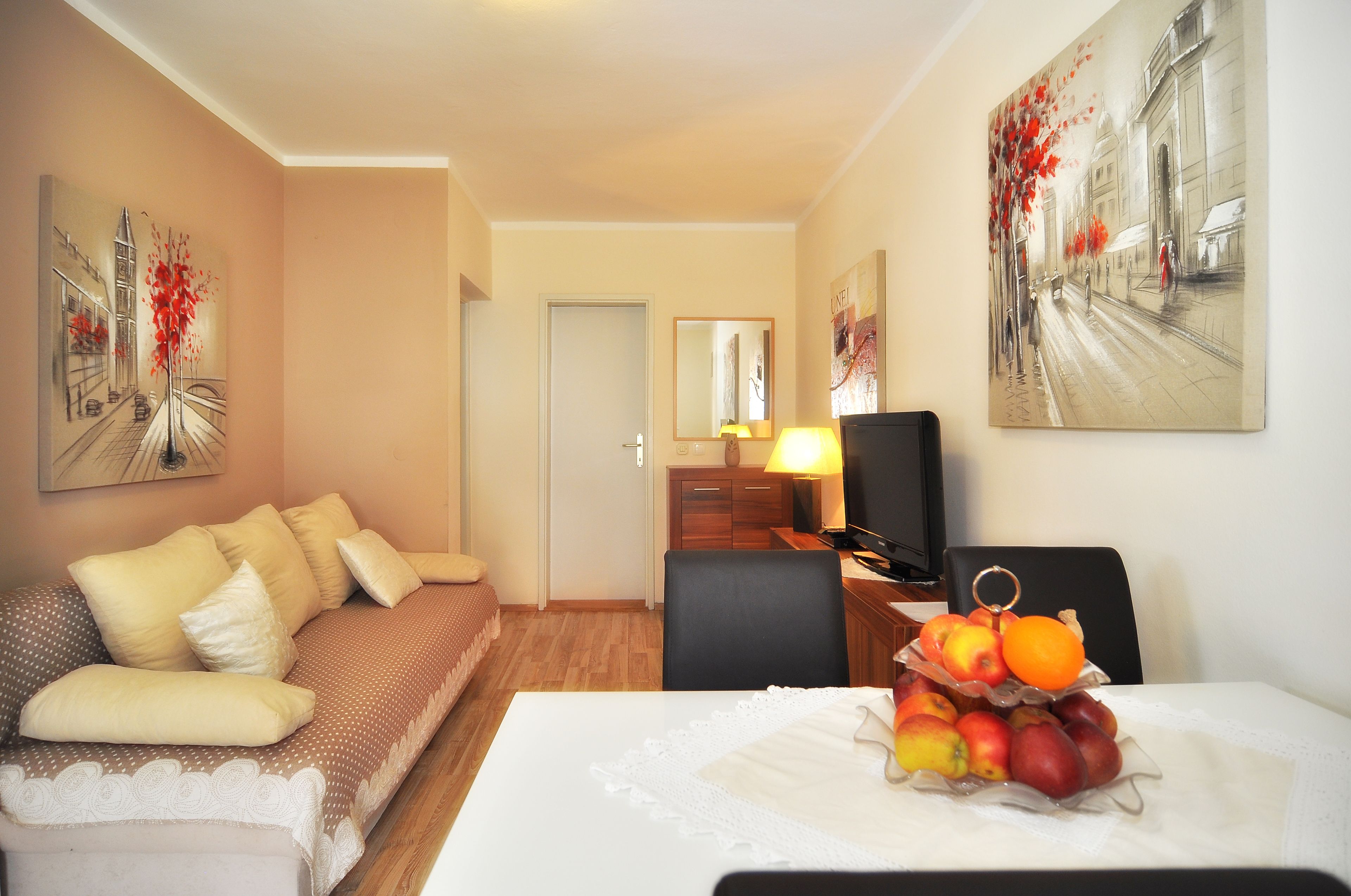 A hotel room with a sofa, a dining table with fruit, a TV, and artwork on the walls.