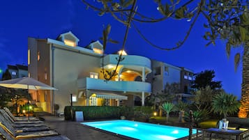 Ein modernes, zweistöckiges Gebäude mit Pool, Sitzgelegenheiten im Freien und einem gut beleuchteten Eingangsbereich.