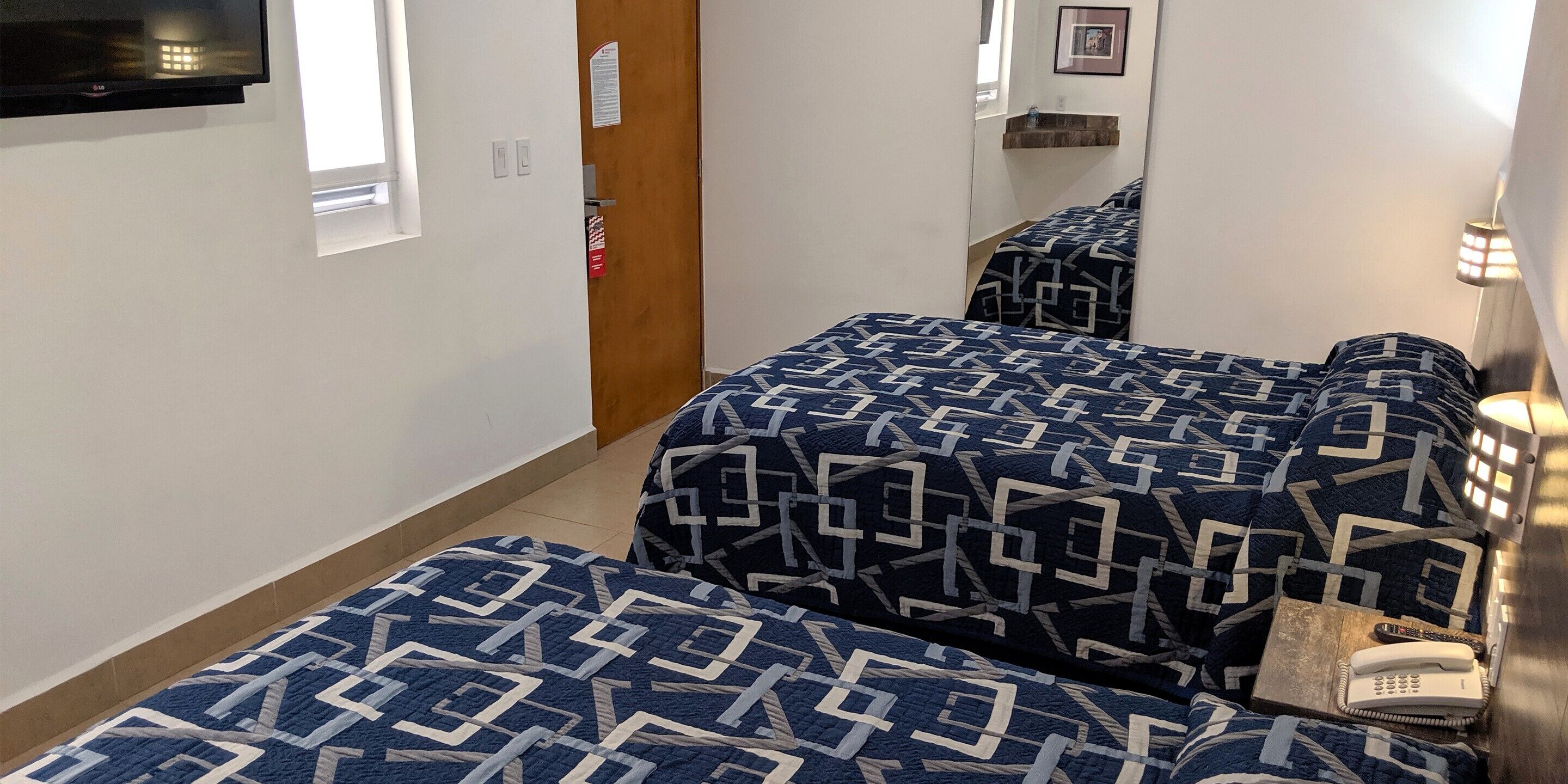 A hotel room with two beds, a flat-screen TV, a bedside lamp, and a telephone.