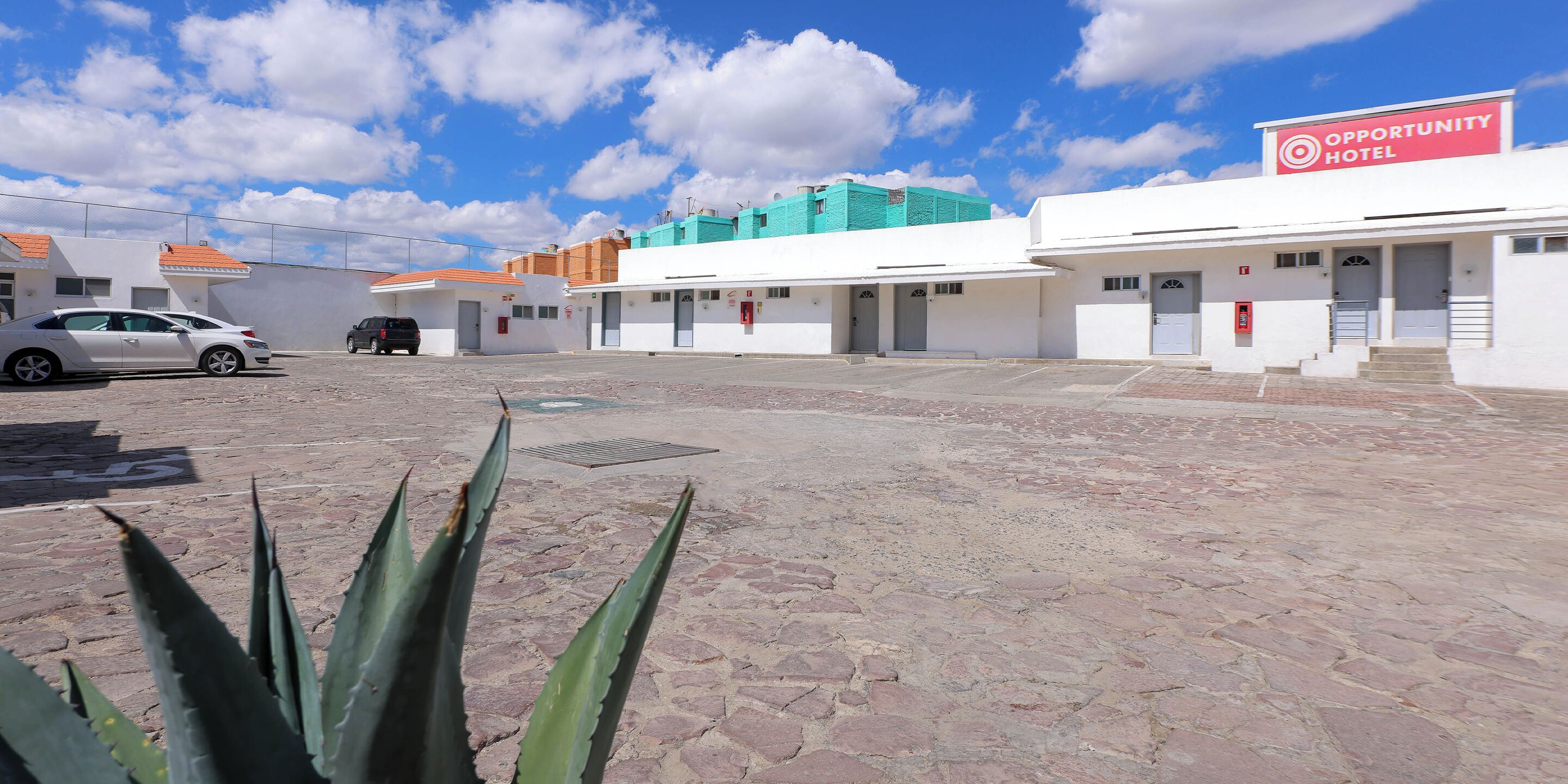 Un hotel con un letrero que dice "Opportunity Hotel", que presenta un patio con pavimento de piedra y algunos automóviles estacionados.